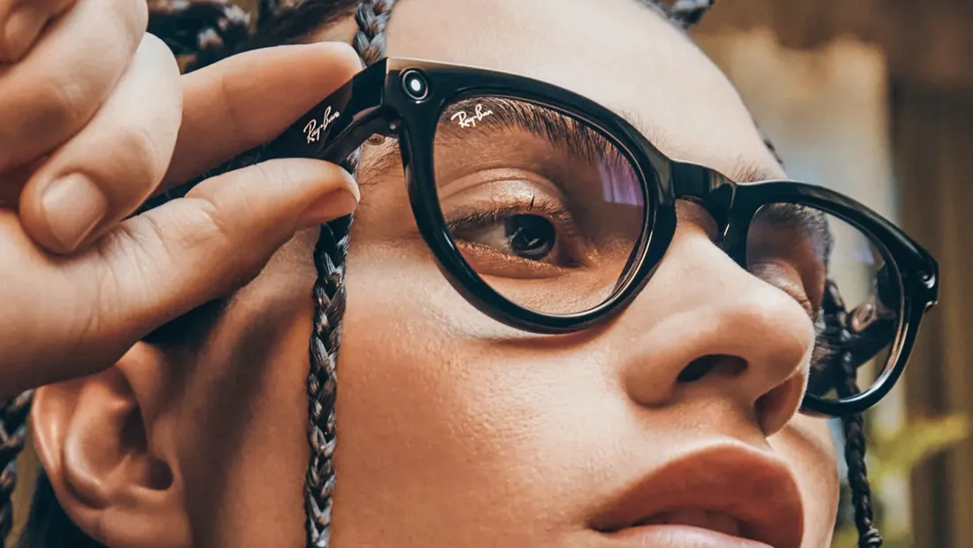 Person wearing clear-frame Ray-Ban Meta smart glasses with the camera and indicator light visible on the temple