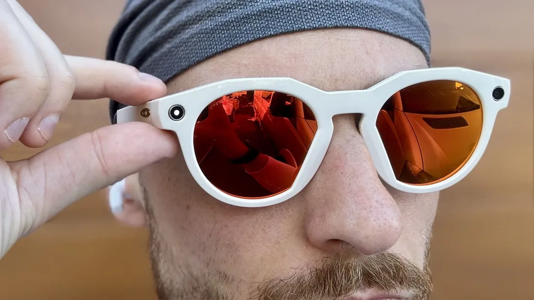 Person holding up white Oakley Meta HSTN smart glasses with the camera and indicator light visible on the temple
